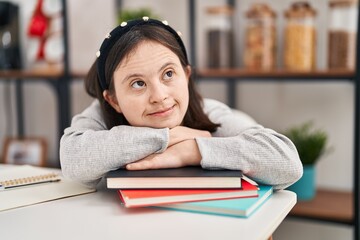 Young woman with down syndrome leaning on books sitting on table at home