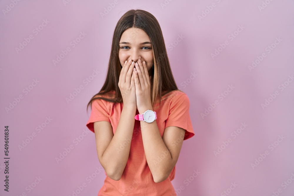 Sticker Teenager girl standing over pink background laughing and embarrassed giggle covering mouth with hands, gossip and scandal concept