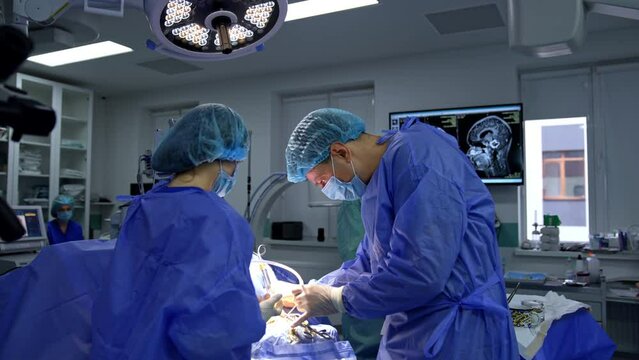 Neurosurgical operation conducted in the modern well-equipped operational room. MRI image of head on the black screen at backdrop.