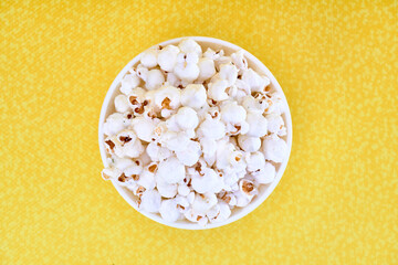 a white bowl of salted popcorn on a yellow background with copy space for advertising. top view