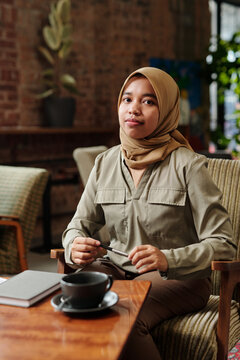 Young successful African American Muslim female employee or intern in hijab and casualwear sitting in armchair and organizing work