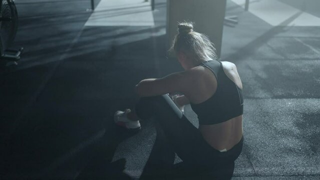 tired sportswoman crying after hard training in gym, sitting on floor alone, suffer by pain in body