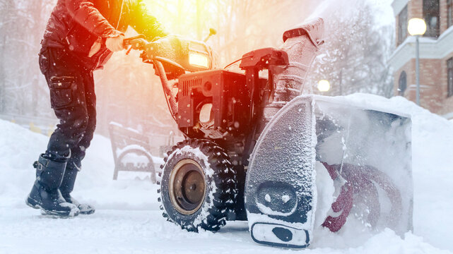 a janitor on a snowplow removes snow in the courtyard of a residential building