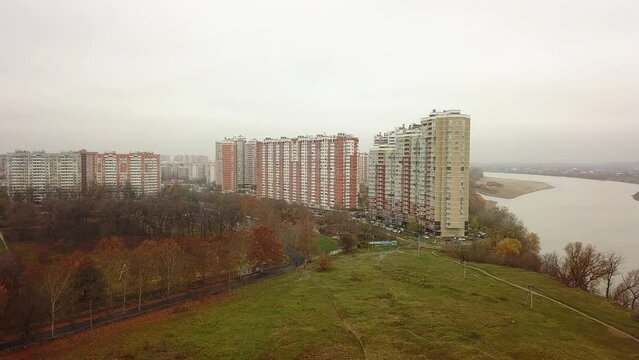 aerial view of a field and a wasteland on the outskirts of a  city with high-rise buildings of modern architecture near a wide river on an autumn cloudy and rainy day