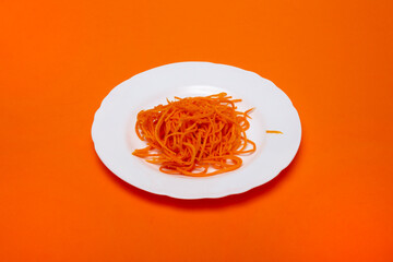 Thinly sliced carrots on a white plate on an orange background