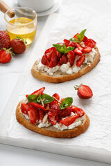 Appetizer with ricotta cheese, cream cheese, honey, strawberry, mint on white board and marble table. Toast, snack, bruschetta. Sweet Sandwich.