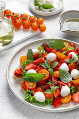 Diet and healthy salad with cherry tomatoes, mozzarella cheese, strawberry, basil and olive oil on grey background.