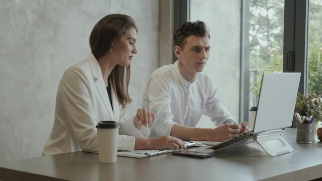 Two young coworkers communicating with online colleague while female economist making presentation of document with financial data at digital meeting