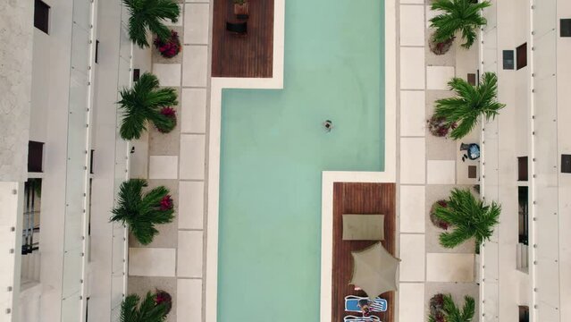 A girl in swimsuit dives in a swimming pool of a luxury boutique hotel and residence complex with penthouses made by Blue Luxury developers in TULUM Mexico, slow cinematic top-down aerial view reveal