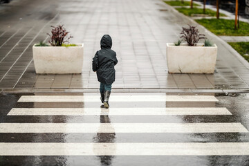 A little boy in hurry is walking across the crosswalk on the rainy day.