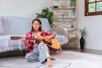 Hobby concept, Young asian woman wearing headphone and sit on the floor to playing acoustic guitar