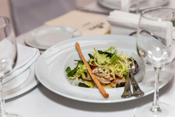 An appetizer of poultry meat and lettuce on a plate on a festive table with a white tablecloth. Appetizing appetizers. Close-up.