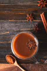 Hot cocoa in cup glass with cinnamon stick, star anise and cocoa powder on wooden background, Hot drink in winter season, Table top view