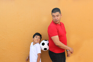 Latino dad and son share their love for soccer, they take a ball with their hands excited to watch the football game © Arlette