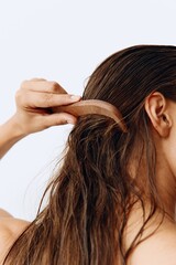 A woman with long brown hair stands back and takes care of her hair after washing and combing her hair with a wooden comb. Healthy hair without hair loss
