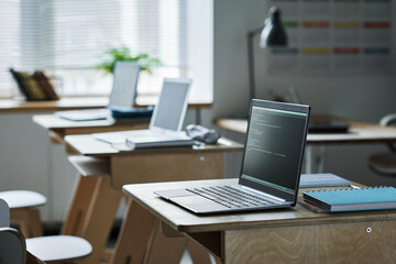 Computers with coding on screens standing on desks in class for studying IT technology