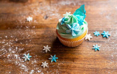 Homemade cupcake of blue color placed on wooden desk. Winter and christmas theme, snowflakes on cream with blue ice. Fresh and home baked sweet.