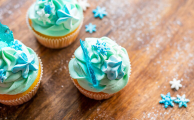 Homemade cupcake of blue color placed on wooden desk. Winter and christmas theme, snowflakes on cream with blue ice. Fresh and home baked sweet.