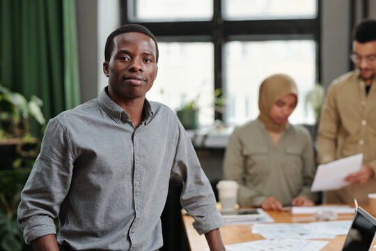 Young confident African American business leader in smart casualwear standing in front of camera against two intercultural colleagues