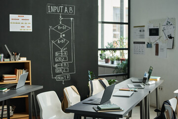 Modern classroom with computers on table for studying IT technology with blackboard with charts in background