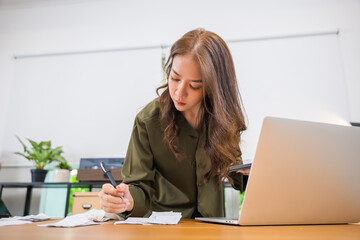 Asian young woman working with financial data she calculator with tablet computer and writing make note calculate, female calculating family budget financial and accounting, pay bills tax online