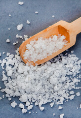 Coarse salt with wooden scoop on grey surface with copy space