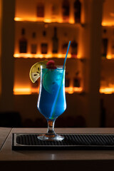 Glass of Blue Lagoon cocktail decorated with lime at bar counter background.