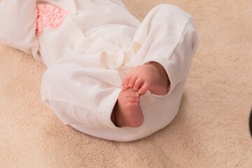 Closeup shot of newborn baby's feet, wearing bodysuit with diaper comfortable lying at home, newborn chubby leg bodypart movement in bed, healthy infant girl try to move tiny feet, childbirth concept.