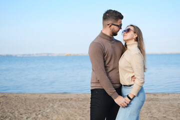 Beautiful young couple posing against the blue sky and water. Couple holding hands and looking at each other