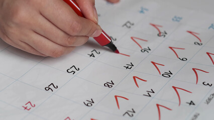 Blurred calendar page. Close-up female hand cross out days in calendar. Red circle marked with pen...