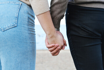 Young man and woman hold hands while walking along the beach. Hands shot close up
