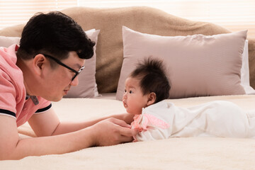 Selective focus father and healthy newborn 3 months baby eye contact together on bed, happy dad spent time talk to daughter at home. toddler infant prone by herself look to dad lift head up.