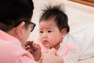 Closeup of newborn baby 3 months  eye contact with happy father with love and happiness, dad play with adorable daughter on bed, toddler infant newborn prone by herself look to dad. fatherhood concept