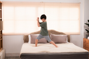 Fototapeta na wymiar Happy asian elementary school boy jumping and dancing on bed, kid jumped and stomped around joyfully alone in bedroom without feeling tired. little boy have fun on the weekend. healthy child concept.