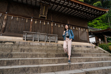 low angle shot with full length of stylish asian Japanese woman tourist walking down the stone stairs at honden main hall of ujigami jinja shrine in uji Kyoto japan