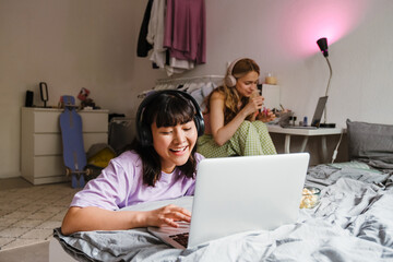 Two multiracial girls listening music and using laptops at home
