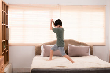 Fototapeta na wymiar Happy asian elementary school boy jumping and dancing on bed, kid jumped and stomped around joyfully alone in bedroom without feeling tired. little boy have fun on the weekend. healthy child concept.