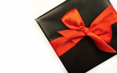 Gift box wrapped in black paper with a red bow. White background. Holiday concept. Place for text or advertising. Christmas. Valentine's Day.