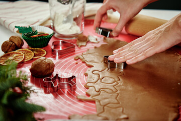 Woman preparing gingerbread cookies at kitchen with Christmas decorations. Female hands cutting ginger dough with cutter to making cookies for winter holidays