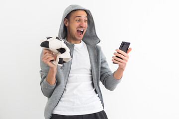 Handsome player man playing soccer holding football ball over background with surprise face...