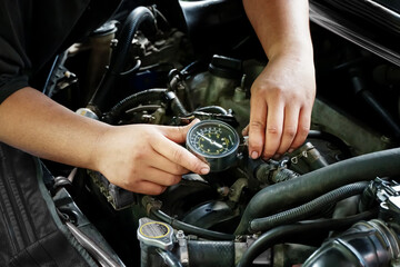 Male mechanic measures the compression in the cylinder of a car engine using a barometer and repair in a workshop for vehicles. Auto service industry. engine compression tester.                     