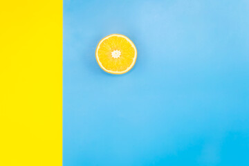 Half of an orange on a blue and yellow background, flat lay, minimalism.