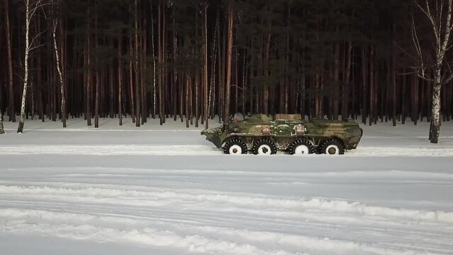 armored personnel carrier moves through the snow along the forest