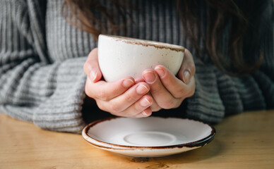 Close-up, a white cup in female hands on a blurred background.