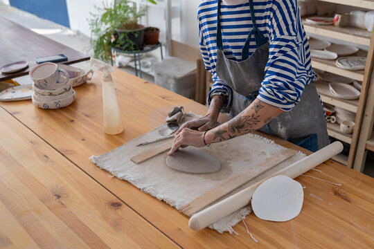 Closeup of female ceramics master create craft plate of wet pot. Table of pottery workshop owner with material for shaping handicraft tableware. Art therapy for mental health concept