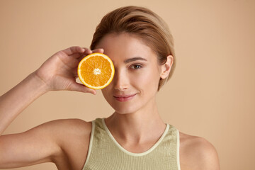 Beautiful Woman Smiling with Orange Fruit. Positive Woman with Radiant Face Recommended Vitamin for Skin. Girl Model with Natural Makeup and Glowing Hydrated Skin. Vitamin C Cosmetics Concept  - 549647075