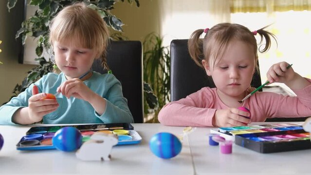 Happy sweet little girls kids, decorate eggs with paints. Preparation for Easter.
