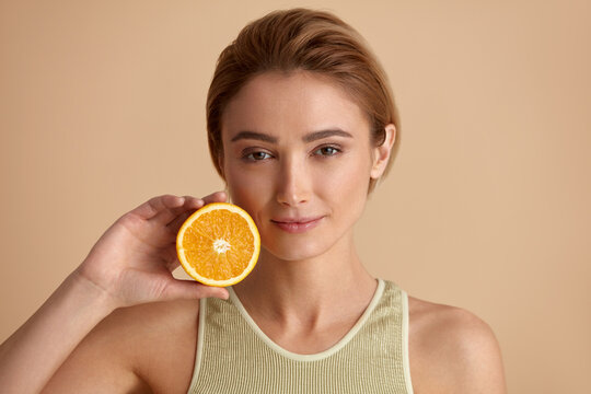 Beautiful Woman Smiling with Orange Fruit. Positive Woman with Radiant Face Recommended Vitamin for Skin. Girl Model with Natural Makeup and Glowing Hydrated Skin. Vitamin C Cosmetics Concept 