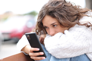 Sad woman checking phone sitting in a bench