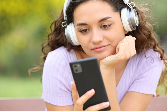 Woman listening to music in a park checking phone